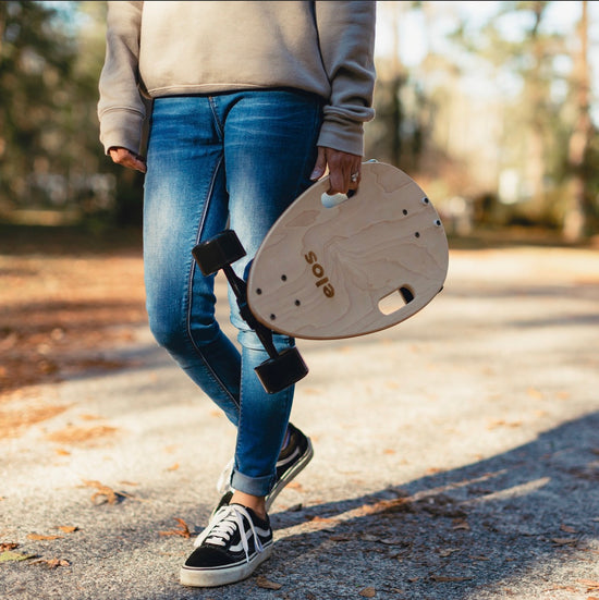 A girl holding Elos skateboards, strolling in park at sunset