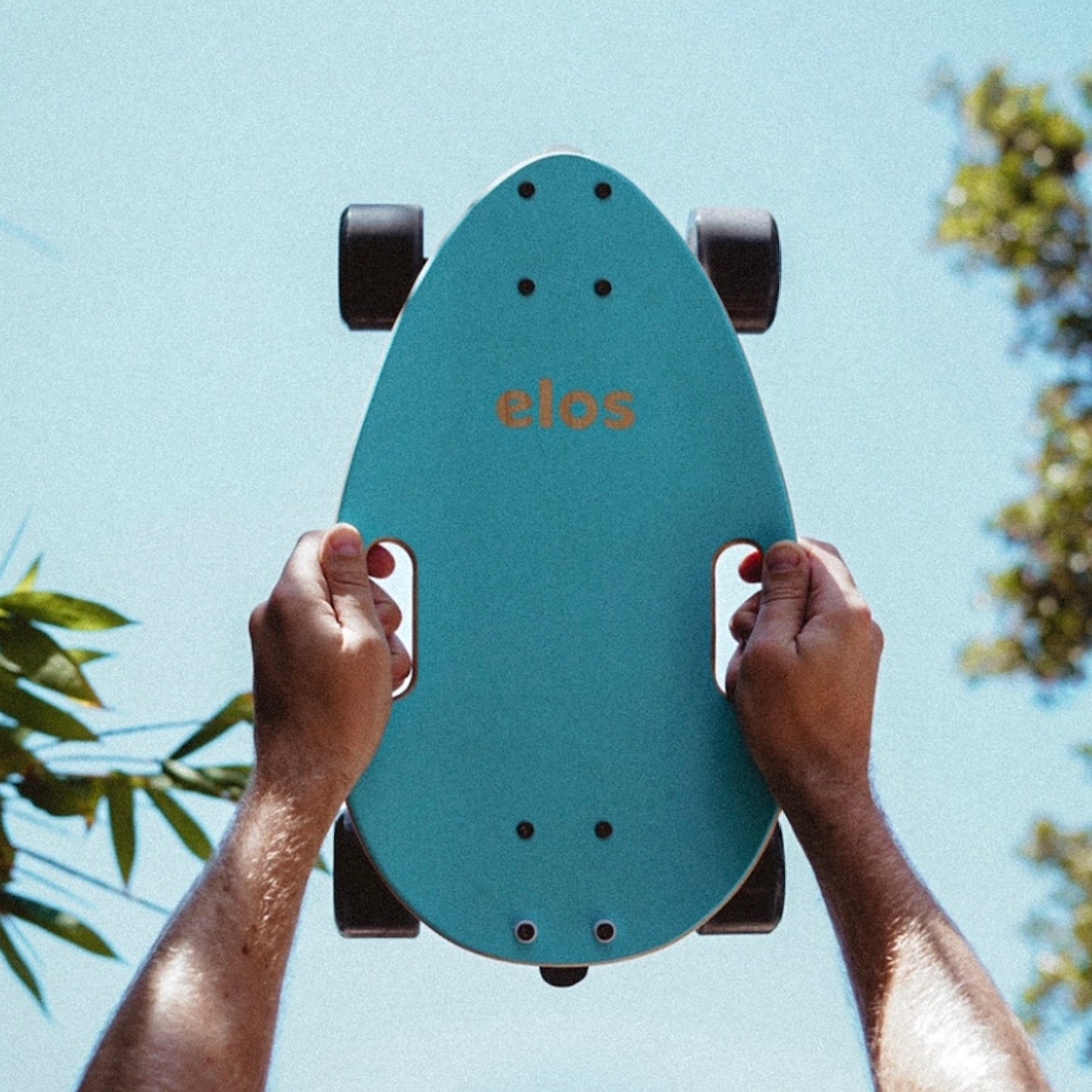 A woman holding green Elos skateboards against a sunny sky backdrop