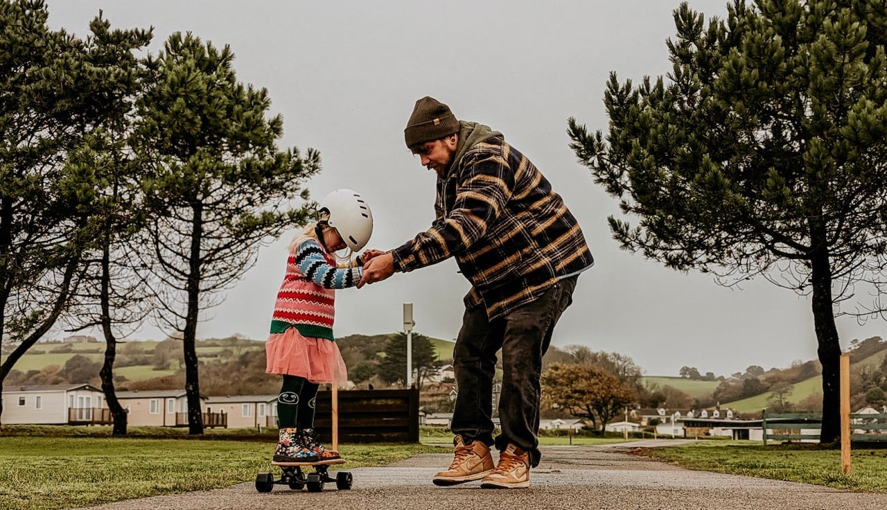 A father teaching daughter how to skate Elos skateboards on winter Sunday afternoon