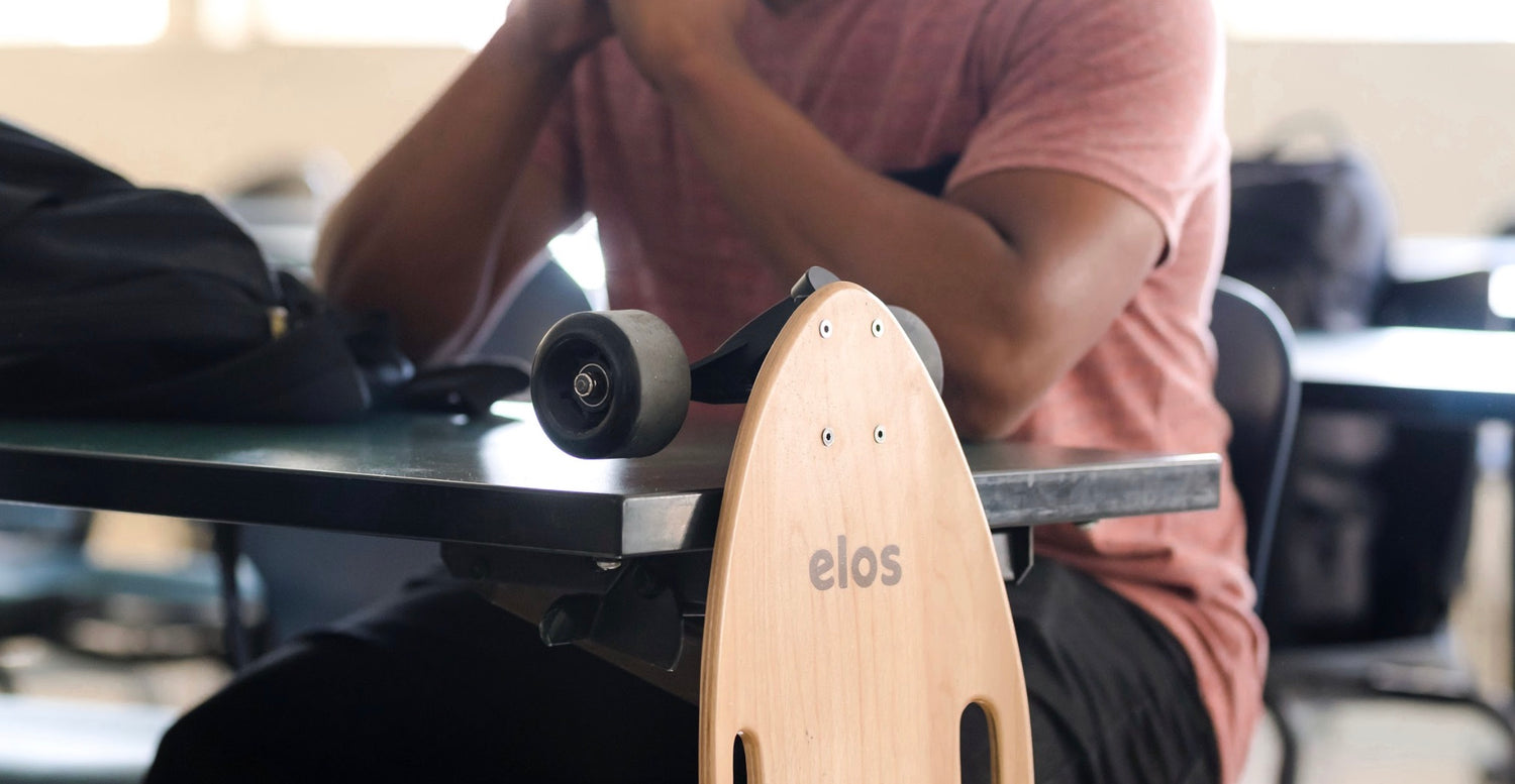A man sitting in the class room while Elos skateboard is hanging next to him