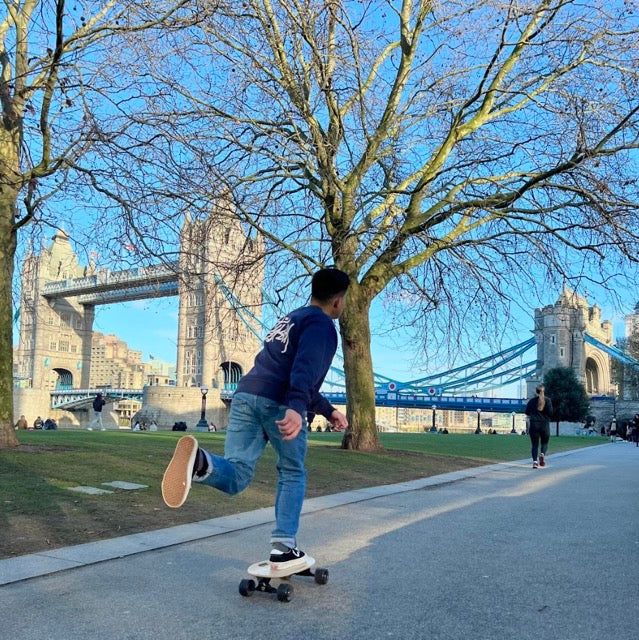 An Asian man showcases his skills with an Elos longboard skateboard near London Bridge, an iconic location for skateboard enthusiasts