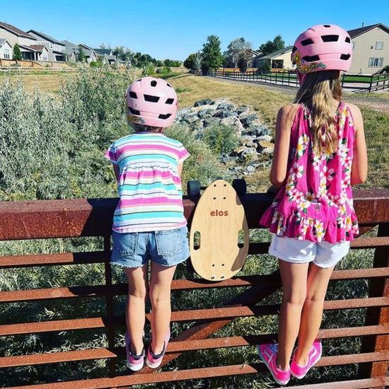 Two girls watching scenery of uk countryside with maple Elos skateboards hanging on fence next to them